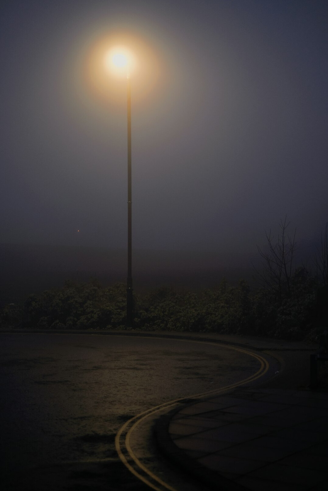 Foggy empty street at night with a single lamppost